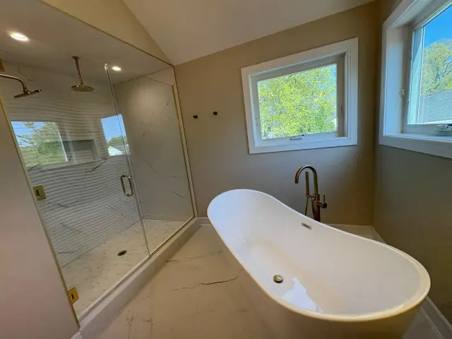 A freestanding tub with a brass faucet beside a glass-walled shower