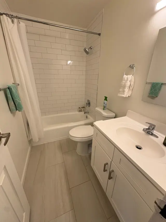 A bathroom with a subway-tiled tub, white vanity and tile floor