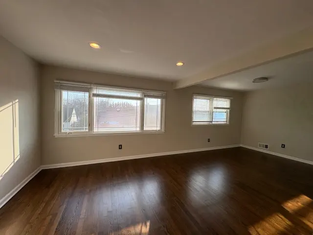 An empty living room with recessed lights and dark hardwood floors