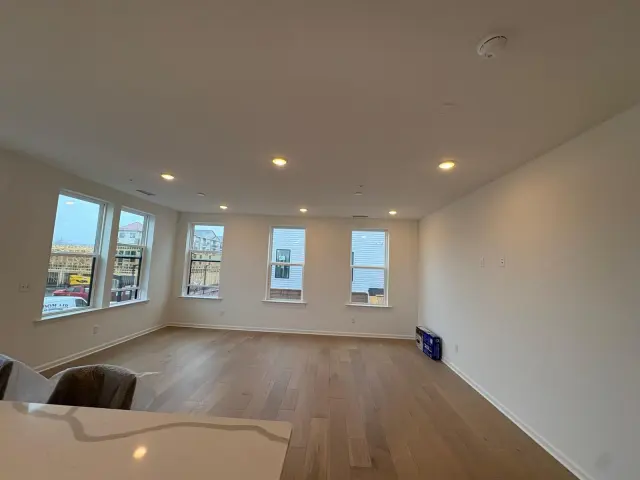 An empty living room with wide plank floors and a row of windows