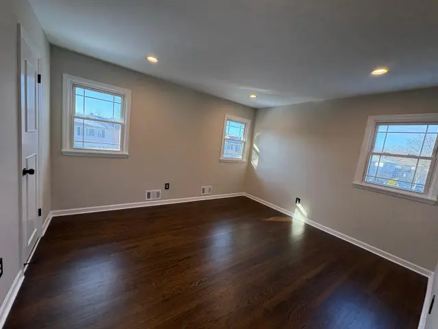 An empty room with three windows and polished dark hardwood