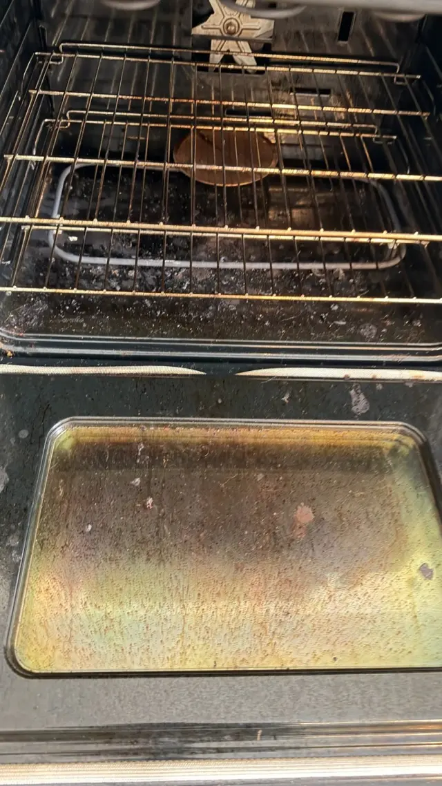 An oven before cleaning, with grease and burnt-on buildup on the racks and floor