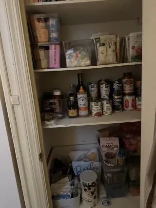 The same pantry after organizing, with cans, jars and snacks sorted into clear bins