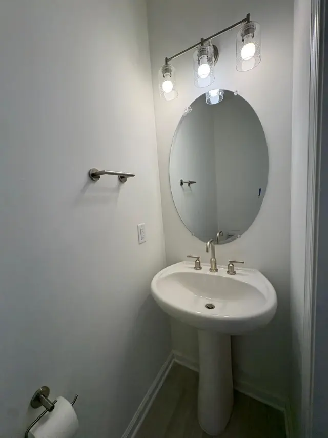 A powder room with a pedestal sink, oval mirror and wall light