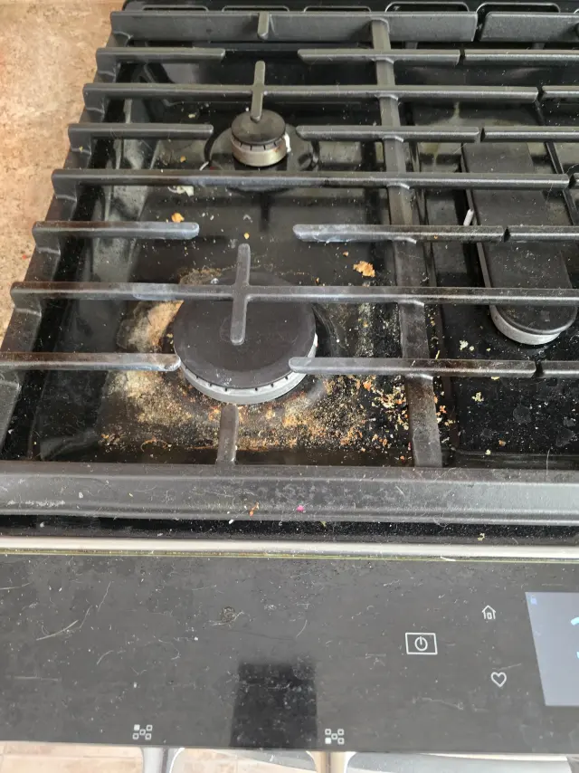 A gas stovetop before cleaning, with crumbs and grease around the burners