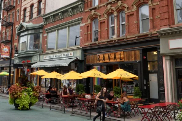 Yellow umbrellas over pavement cafe tables outside brick storefronts